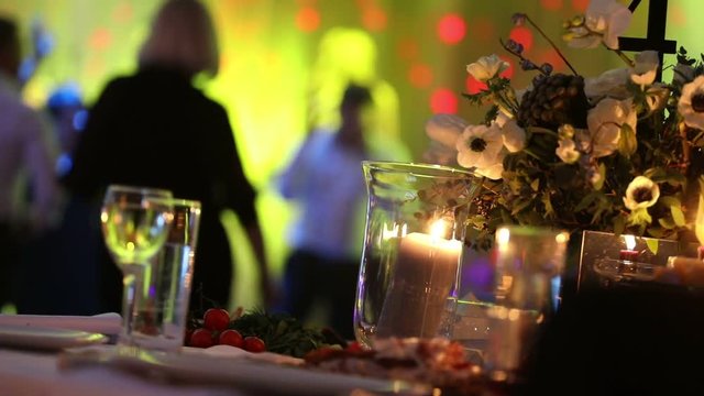 Group of silhouetted people dancing in a dark banquet hall for a wedding reception.The Wedding Banquet, people dance - shot through the wedding table decorations, wedding decoration