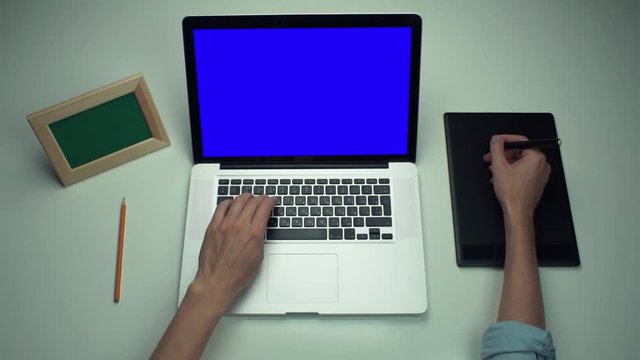 Man using digital graphic tab and laptop with green screen at white desk