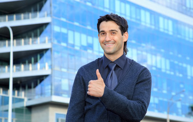 Handsome man smiling while standing against business office building background. Thumbs up happy man.