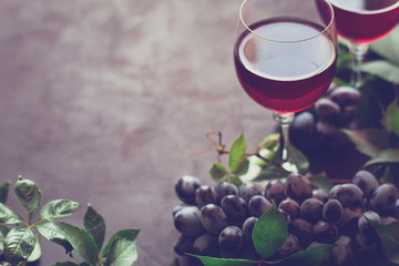 Still life with wineglasses, bottles, grapes and leaves on brown wooden desk