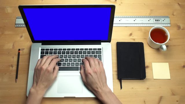 Top view male hands using laptop with green screen at wooden desk