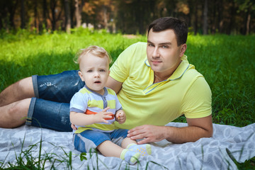 Fototapeta na wymiar handsome guy resting with his son in forest, healthy young man playing with little son in city park