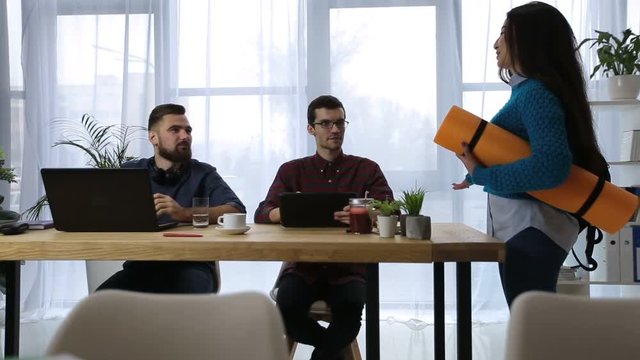 Charming asian office woman with exercise mat going to fitness training after work. Sporty female colleague asking permission from hipster boss to leave work early for yoga in startup office. Dolly