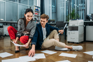 young business partners doing paperwork while sitting on floor at office