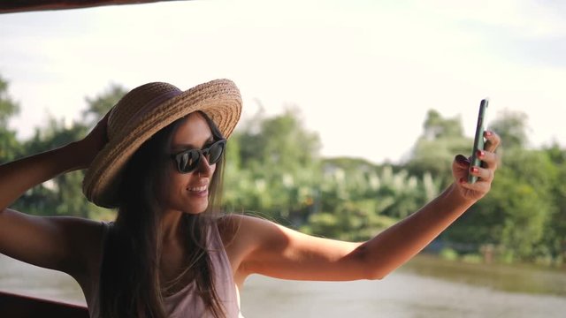 Beautiful Mixed Race Tourist Girl in Big Hat Taking Selfie Photo Using Mobile Phone and Cruise on Boat at River in Thailand. 4K Slow Motion.