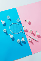 top view of shuttlecocks around badminton racket on blue and pink papers