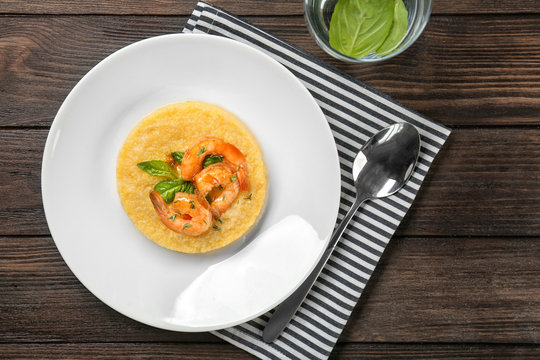 Plate with fresh tasty shrimp and grits on wooden table, top view