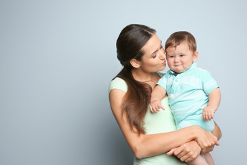 Young mother with little son on color background