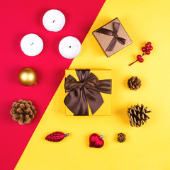 Colorful flatlay with various Christmas items, decor and gifts, including gift boxes, candles, pine cones etc. Red and yellow background. Christmas concept, square