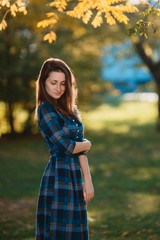 Fashion outdoor portrait of gorgeous long hair woman in long checkered blue dress - spring style. Fashionable young girl in trendy clothes posing at city park