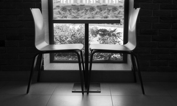 Two modern style chairs near the cute little table near the window with brick wall black and white interior shot