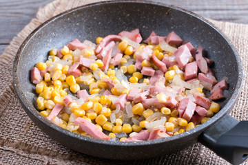 Filling for a pie in a frying pan. Bacon, onion and corn