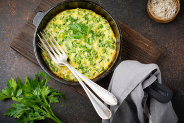 Fritatta with potatoes, green peas and herbs in an iron frying pan on dark concrete or stone background. Selective focus. Rustic style