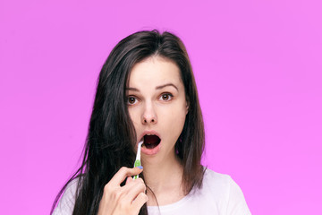 Young beautiful woman on a pink background brushes teeth