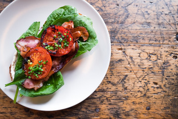 Plate with BLT toast with grilled tomatoes, bacon, lettuce and special sauce on the old wooden table top view