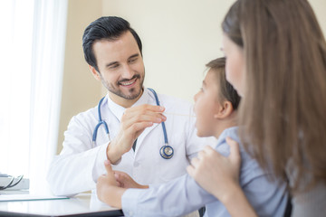 Attractive doctor man checking to inside boy mouth at clinic. Doctor working with attractive smile.