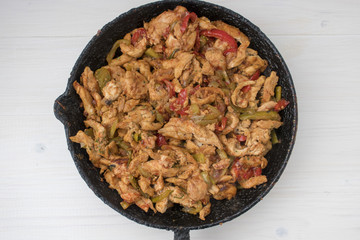 Chicken stew with red and green pepper, with red onion, pickled cucumber and spices in a frying pan.