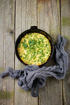 Fritatta with potatoes, green peas and herbs in an iron frying pan on an old wooden background. Selective focus. Rustic style.Top view.