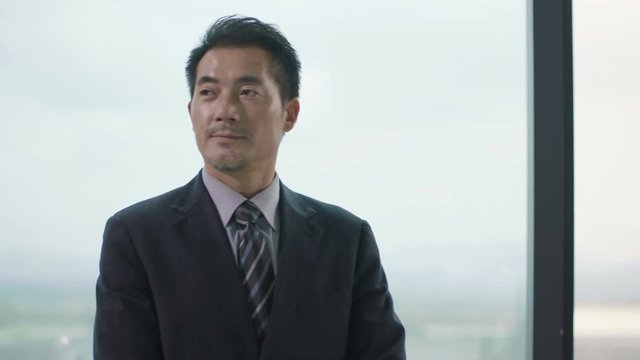 asian corporate executive looking around and thinking in front of window in office
