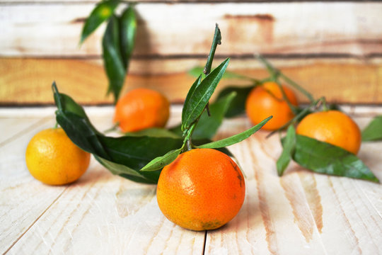 Fresh tangerines with green leaves on colorful wooden background. Scattered fruit on wooden table.