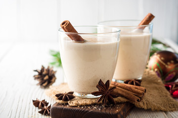 Homemade eggnog with grated nutmeg and cinnamon on white wooden table. Traditional Christmas drink.