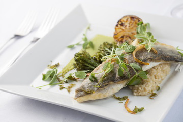 Sea Bass with lemon and vegetables on a square white plate with cutlery