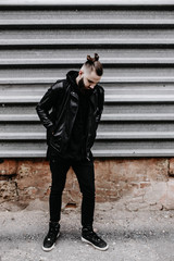 Modern young bearded man in black style clothes standing in around urban background.