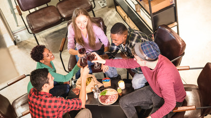 Top side view of multi racial friends tasting red wine and having fun at cool fashion bar winery location - Multicultural trendy friendship concept with people enjoying time out drinking together