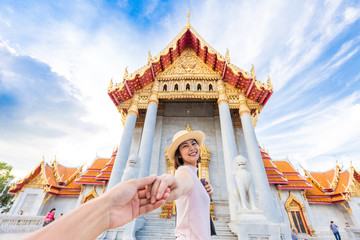 Asian tourist women in hat leading man hand to travel at marble temple
