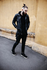 Obraz premium Modern young bearded man in black style clothes is walking at street.