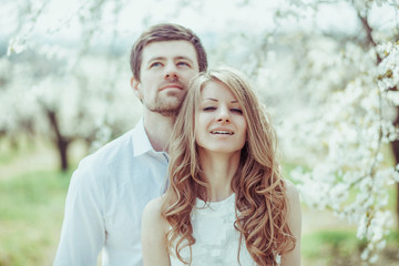 Fototapeta premium Happy Smiling Couple Relaxing in blooming apple tree garden. Man looking up. Portrait horizontal shot