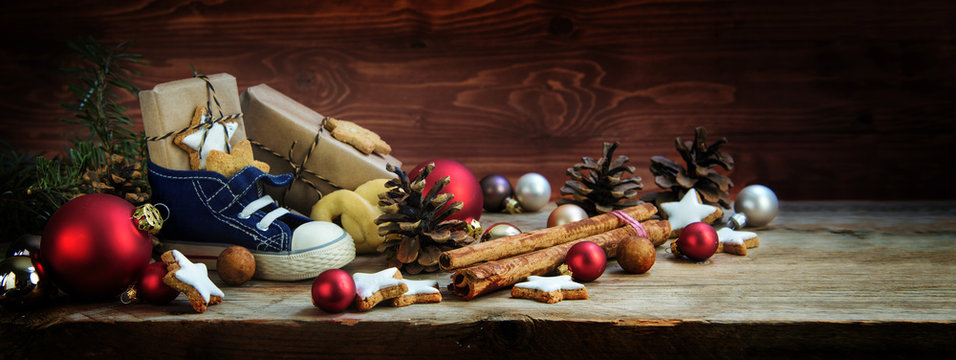 Wide background for St. Nicholas Day, Children's shoe with sweets and gifts on December 6th on rustic wood, german christmas consumption called Nikolaus, panoramic format, copy space