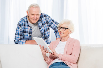 portrait of senior woman using tablet while husband standing near by at home