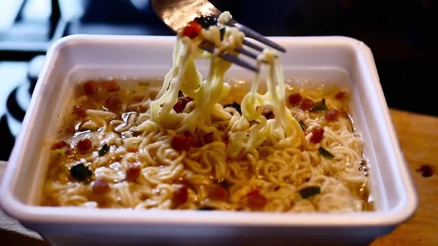 The process of preparing instant noodles with spices, vegetables, and meat. Slow motion of pouring boiling water into the instant noodles, stirs instant noodles with a fork.