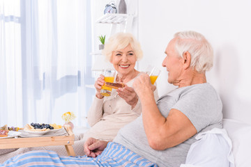 happy senior couple having breakfast in bed together at home