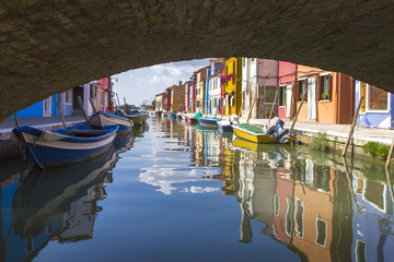 Fototapeta na wymiar ENICE, ITALY - JUNE 28, 2013: View of the colorful Venetian houses and boats with reflection along the canal at the Islands of Burano in Venice.