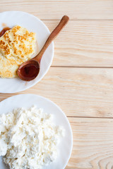 Two white plates with fresh curd and cheesecakes on wooden table with copy space. Top view.