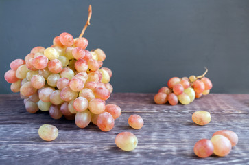 Two big and small tassels of ripe green-red grapes and some berries are lying on the dark wooden table.