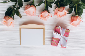 Blank paper note with envelope, gift and pink rose on wooden background.