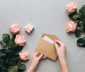 Female hands open a letter with propose and hold a wedding ring on a gray background.