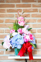 Artificial flower in the pot over wood table , brick wall background