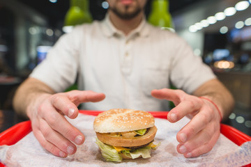 A man takes a large burger who is standing on the tray. Hands are drawn to the tasty cheeseburger. Focus on the burger.