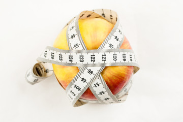 Ripe red juicy apple with measuring tape around it on a white background