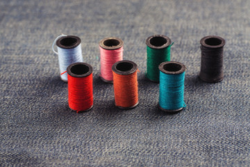 Different colour threads on splools on a piece of jeans fabric