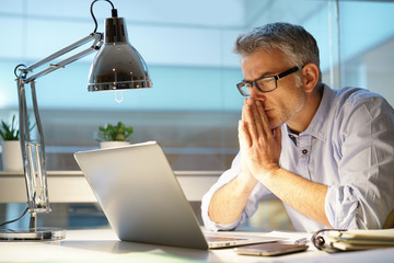 Businessman in office being thoughtful in front of laptop