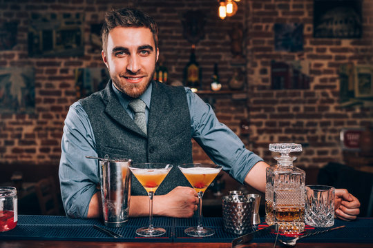 Handsome smiling bartender enjoying work and preparing cocktails at bar