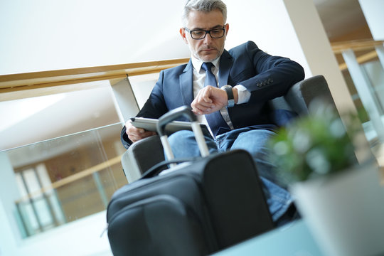 Businessman in airport lounge checking time on watch