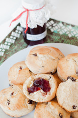Freshly baked traditional British Buttermilk scones with raisins on white plate with cloth napkin and jar of homemade red currant jelly or jam on green vintage metal tray with rust on white table