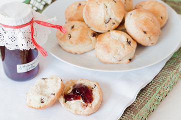 Freshly baked traditional British Buttermilk scones with raisins on white plate with cloth napkin and jar of homemade red currant jelly or jam on green vintage metal tray with rust on white table