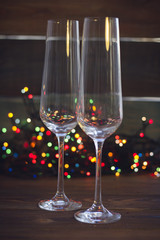 A festive still life with two empty champagne glasses on a dark colored wooden background. Dark colorful bokeh